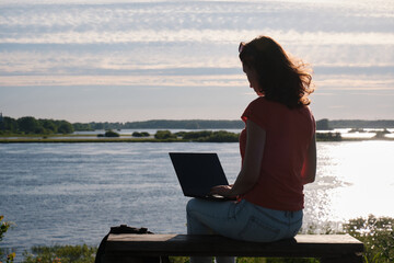 The girl sits on a bench and uses a laptop. Communication outside the city. Camp