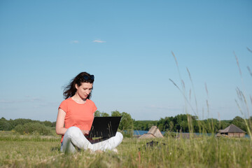 Naklejka na ściany i meble The girl sits on the grass and uses a laptop. Communication outside the city. Ca