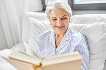 Fototapeta na wymiar technology, old age and people concept - senior woman reading book in bed at home bedroom