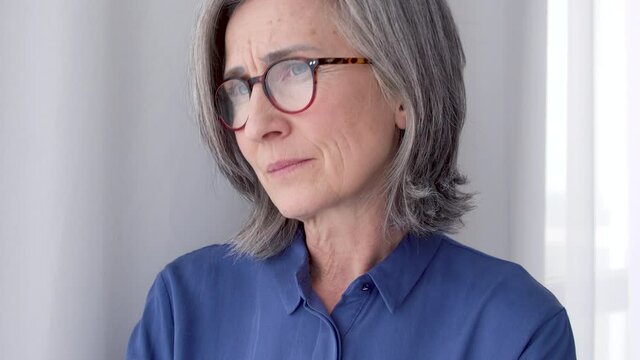 Upset middle aged woman in red eyeglasses sadly looking at window, feeling bad