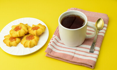 White cup with tea and homemade cookies, kitchen cotton napkin on a bright yellow background. Concept of breakfast, afternoon tea. Top and side view