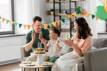family, holidays and people concept - portrait of happy mother, father and little son with four candles on birthday cake clapping hands at home party party