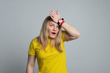 Photo of woman regrets wrong doing, keeps hand on forehead, dressed in casual yellow t shirt