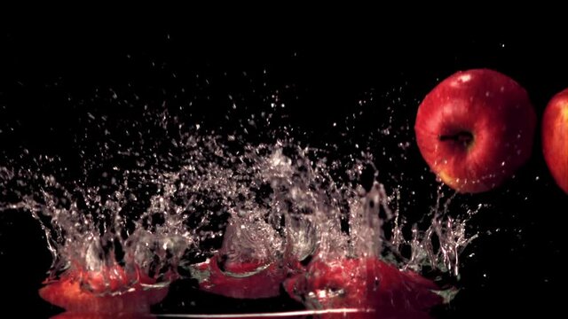 Super slow motion red apples fall on the water with splashes. On a black background. Filmed on a high-speed camera at 1000 fps. High quality FullHD footage