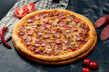 Appetizing pizza with hot jalapeno peppers, salami, sausages, red sauce and parmesan cheese. Dark background. Italian Cuisine