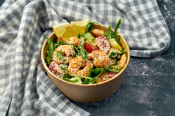 Healthy salad with shrimps, arugula, cucumber, cherry tomatoes and sauce in a delivery package on a dark background. Close up