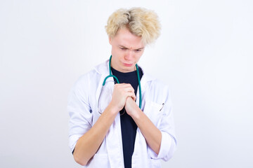 Sad young handsome Caucasian doctor man standing against white background feeling upset while...
