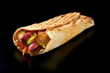 Appetizing shawarma with smoked sausages, cucumbers, carrots and tomatoes in pita bread. Black...