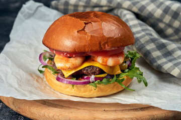 Delicious burger with beef, tomatoes, lettuce, melted cheese and shrimp on white parchment. Dark background. American fast food