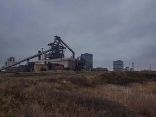 Fototapeta premium The derelict, abandoned hulk of the blast furnace at the Redcar Steelworks against a clouded sky, seen from the dunes of Coatham Marshes.