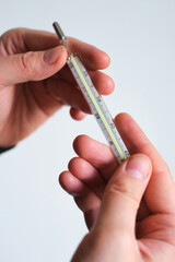 Medical thermometer close-up in the hands of a man. Traditional thermometer for measuring body temperature, Young man measures body temperature. Medicine and health concept