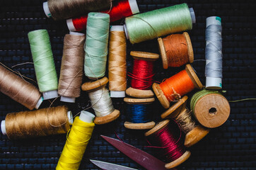 Retro sewing items: tailoring scissors, cutting knife, thimble, wooden thread spools, cushion for including pins, fabrics and sewing accessories.