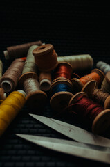Retro sewing items: tailoring scissors, cutting knife, thimble, wooden thread spools, cushion for including pins, fabrics and sewing accessories.