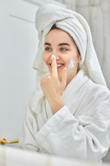 woman in white bathrobes applying apply facial cream