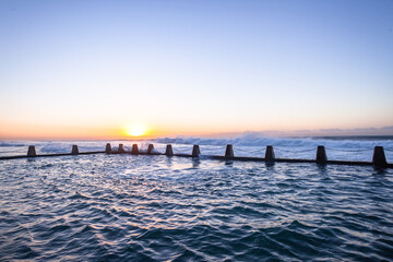 Beach Tidal Swimming pool at dawn sunrise with clear blue sky large ocean sea waves crashing breaking water power from natures weather.