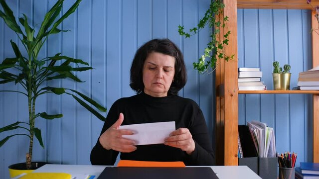 Middle aged woman sit at workplace desk holding papers reading bad news in letter feels frustrated concerned due high taxes, loan debt, dismissal, staff cuts notice, debt eviction notification concept