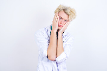 young handsome Caucasian doctor man standing against white background holding head in hands with unhappy expression watching sad movie about animals and trying not to cry.