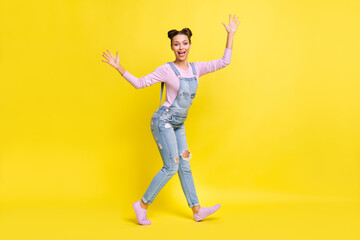 Fototapeta na wymiar Full length photo of charming shiny young woman wear denim overall dancing rising arms hands isolated yellow color background