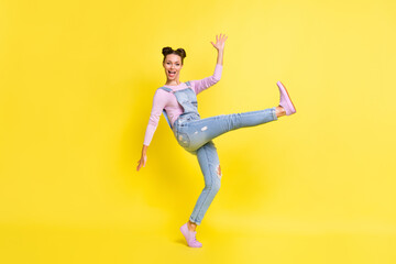 Fototapeta na wymiar Photo of adorable crazy lady stand tiptoe dance raise hand open mouth wear jeans overall shoes isolated yellow background