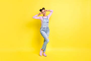 Full size photo of optimistic nice brunet lady show v-sign wear overall isolated on yellow background