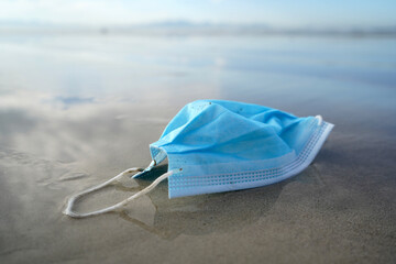 Discarded Covid-19 mask on a pristine beach, medical waste concept