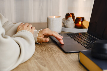 A woman works on a laptop in a cozy environment at home. Freelance girl. Girl in casual clothes. Internet business. Distant work. Girl listens to music on headphones, drinks tea and lights candles