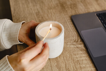 The girl lights a candle at her desk at home. A minute of relaxation after working with a laptop....