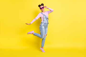 Fototapeta na wymiar Photo of sweet cool young lady dressed jeans overall dark glasses dancing isolated yellow color background