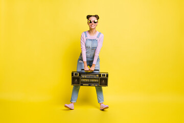 Full size photo of charming cheerful young woman hold boombox smile wear glasses isolated on yellow color background