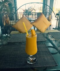 A glass of fruit juice with cocktail straw on the table at the restaurant