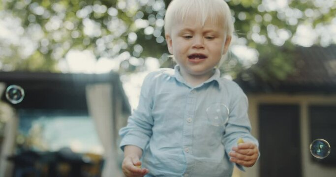 Very interested baby boy, face covered with mosquito bites, watches flying bubbles. Blond hair and clear blue eyes. Cute adorable toddler under 1 year, spending time outdoors, cozy backyard