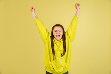 Wow. Beautiful female half-length front portrait isolated on yellow studio backgroud. Young emotional surprised woman standing with open mouth. Human emotions, facial expression concept.