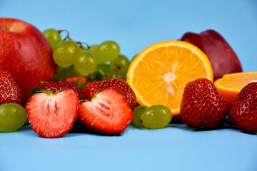 Pile of various fresh fruits on a blue background stock images. Group of fruits isolated on a blue background with copy space for text. Strawberries, grapes, oranges, apples stock photo