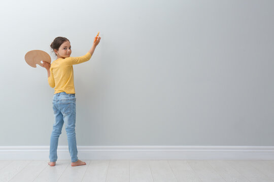 Little girl painting on light grey wall indoors. Space for text
