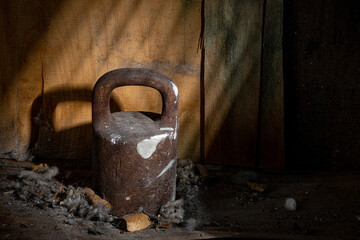 Old metal weight in a pile of dirt and dust on a dark background illuminated by a beam of light