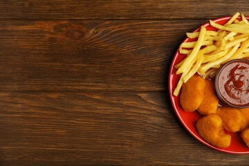 Tasty chicken nuggets and French fries served with ketchup on wooden table, top view. Space for text