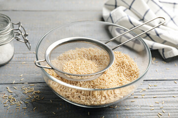 Sieve with rice in bowl on grey wooden table