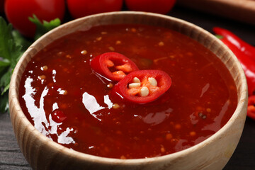 Spicy chili sauce in bowl on wooden table, closeup