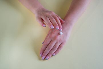 The girl applies a moisturizer to her hand. Close-up on the hands on a yellow background.