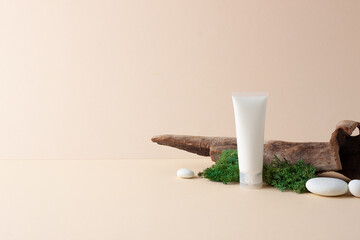 White tube of cosmetic cream with wood and moss on pastel background. Close up, copy space.