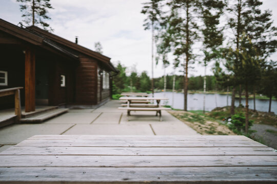 Outdoor wooden table in front if a cottage with a lake in the background and high trees