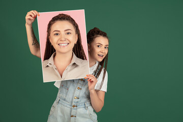 Young girl holding her portrait isolated over green studio background with copyspace for ad. Concept of beauty, fashion.