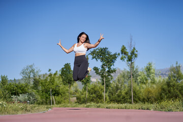 Young woman with fit body jumping. Female model in sportswear exercising and headphones