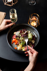 Young woman is eating gourmet  salad in a fancy restaurant with a glass of champagne, female hands in a frame, first person view