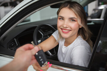 Obraz na płótnie Canvas Beautiful happy woman sitting in her new automobile, receiving car keys from salesman