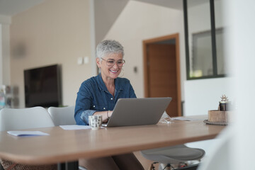 portrait of a 55 year old senior woman working on her laptop in her home