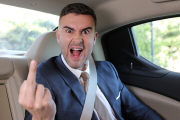 Angry businessman in backseat showing middle finger