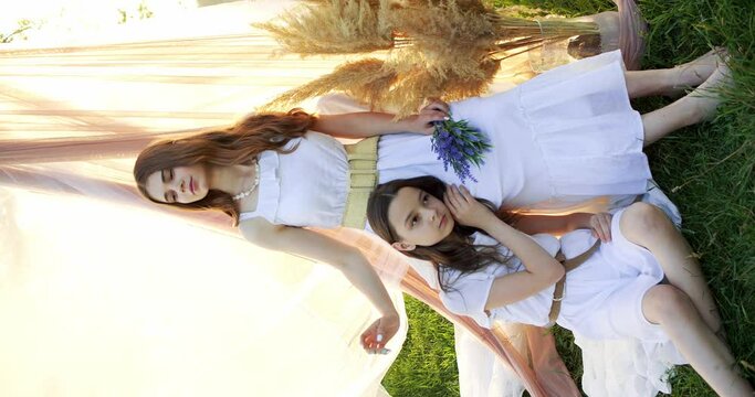 Two girl teenagers in white dresses with flowers bouquet posing on chifon background in a field at sunny summer day