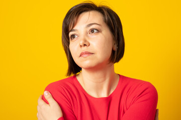 Fototapeta premium Sad young woman wearing casual sweater over yellow background, hugging oneself sad and pensive, smiling confident. Self love and self care.