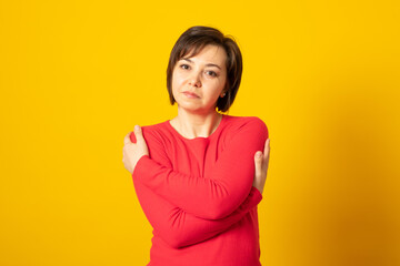 Fototapeta premium Young woman wearing casual sweater over yellow background, hugging oneself happy and positive, smiling confident. Self love and self care.